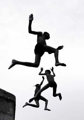 LOW ANGLE VIEW OF MAN JUMPING WITH ARMS RAISED AGAINST SKY