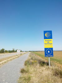 Road sign on landscape against clear blue sky