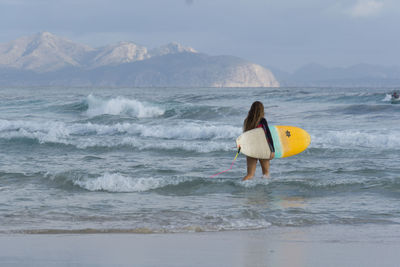 Woman with surfboard walking in sea against sky