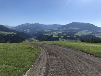 Empty road amidst field against sky