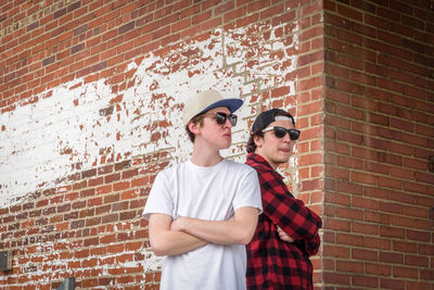 Young man wearing sunglasses standing against brick wall