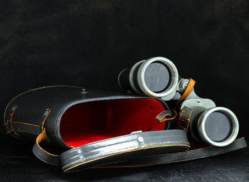 Binoculars and their gray leather case on a black background