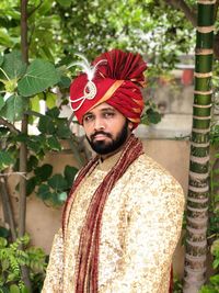 Portrait of bridegroom in traditional clothing standing against plants