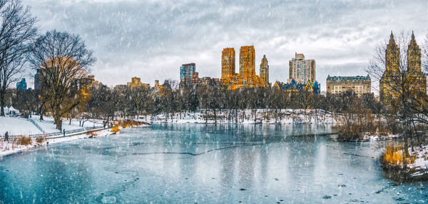 Frozen river by city against sky during winter