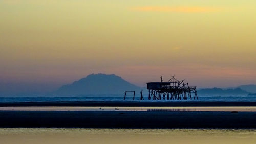 Silhouette built structure on beach against sky during sunset