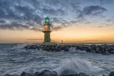 Lighthouse by sea against sky during sunset