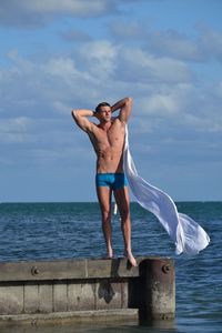 Full length of shirtless man standing on pier in sea against sky