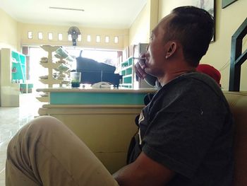 Side view of young man sitting on chair at home