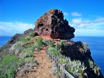 Rock formation by sea against blue sky