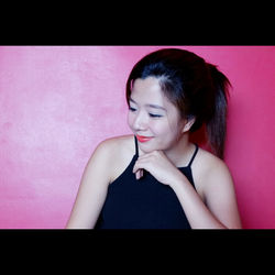 Close-up of young woman standing against pink wall