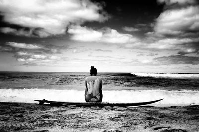 Rear view of woman sitting on surfboard at beach