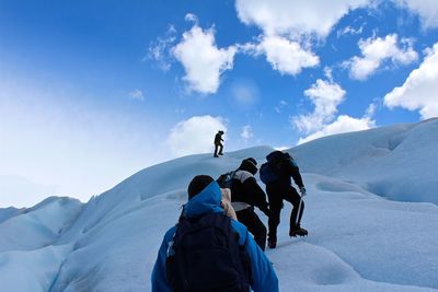 Low angle view of people climbing on snowcapped mountain against sky