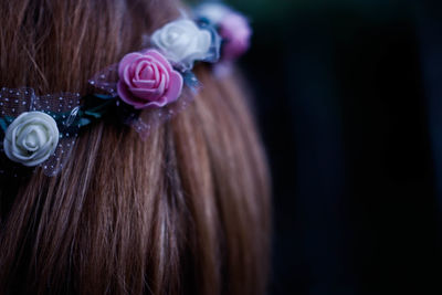 Close-up of woman wearing flowers on hair against black background