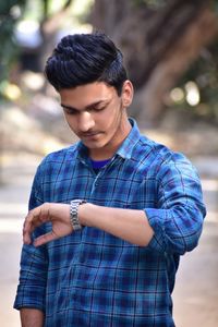 Close-up of young man standing against blurred background and watching in watch