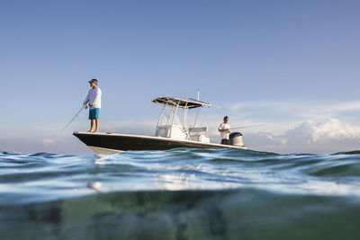 Low angle view of men fishing while standing on boat at sea against sky