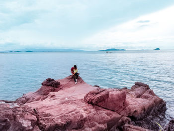 People on rocks by sea against sky