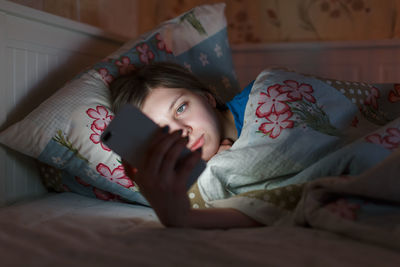 Cute sleepy female in a bed. girl can't sleep, looks into smartphone, suffer from insomnia.