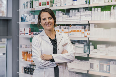 Confident female pharmacist with arms crossed in chemist shop