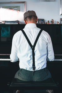 Rear view of man sitting by piano at home