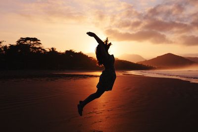 Silhouette of woman standing on beach at sunset