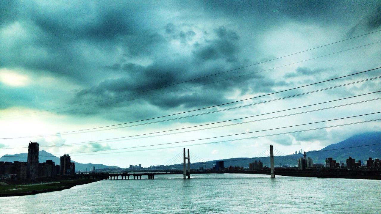 architecture, built structure, waterfront, sky, water, building exterior, city, connection, river, cloud - sky, cloudy, cityscape, bridge - man made structure, cloud, urban skyline, skyscraper, bridge, skyline, outdoors, dusk