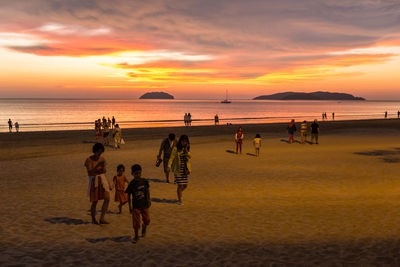 People at beach against sky during sunset