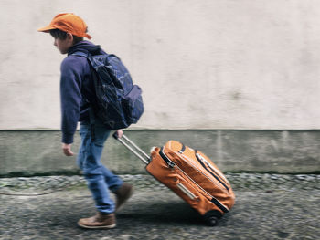 Side view of boy with luggage walking on footpath