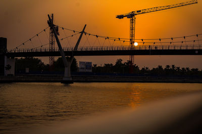 Silhouette cranes by river against sky during sunset