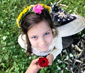 Portrait of girl holding red rose on field