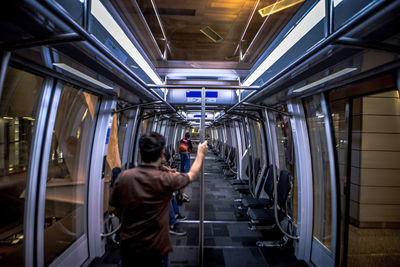 Rear view of man holding pole while traveling in metro train