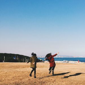 Happy friends dancing on field against clear sky