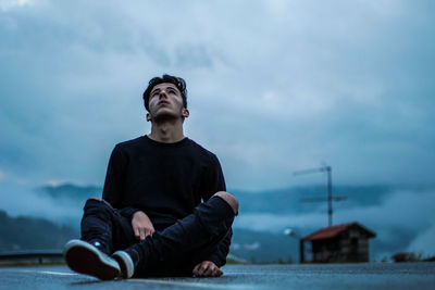 Young man sitting against sky