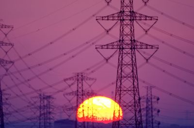 Low angle view of electricity pylon against sky during sunset