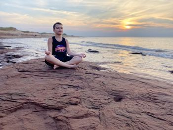 Portrait of young woman sitting on rock at beach