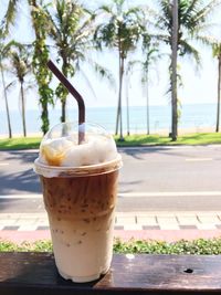 Iced coffee in disposable cup against coconut palm trees