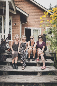 Portrait of happy female friends sitting on wooden steps against house