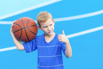 Boy gesturing and holding basketball while standing on sports court