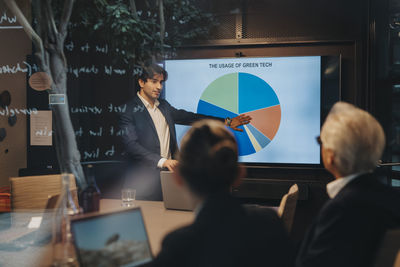 Young businessman explaining pie chart to male and female colleagues during business meeting