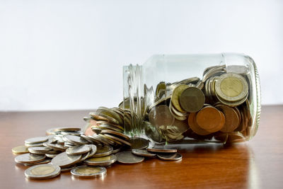 Close-up of coins with jar against white background on table