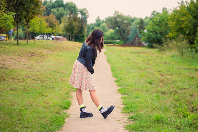 A slender dark-haired girl examines her shoes while standing on a path in the park
