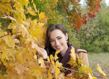 Portrait of woman wearing coat standing by trees in park during autumn