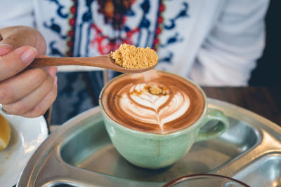 Close-up of hand holding brown sugar over coffee cup