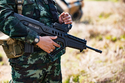 Midsection of male army soldier holding rifle while standing on field