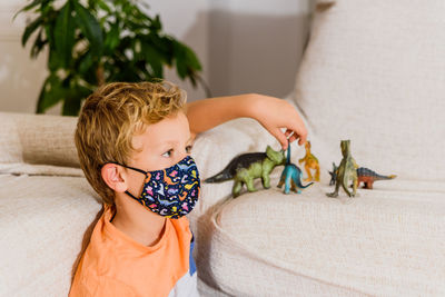Close-up of boy wearing mask playing with toy on sofa