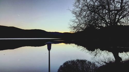 Silhouette trees by lake against sky during sunset