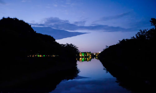 Silhouette trees by lake against sky at night