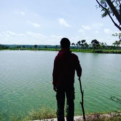 Rear view of man standing by lake against sky