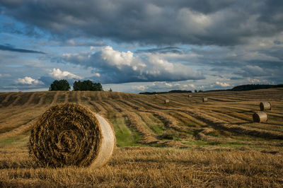 Hay bales on grassy field against cloudy sky