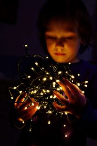 Portrait of boy holding illuminated christmas lights at home