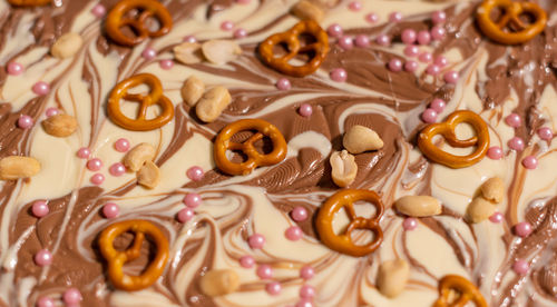 White and brown chocolate prepared for a broken chocolate topped with pretzel, sugar pearls and nuts